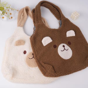 May include: Two plush tote bags with bear faces. One bag is brown with a white bear face and the other is white with a brown bear face.