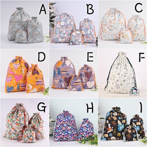 Op de afbeelding: Een verzameling trekkoordtassen in verschillende maten, elk met een uniek bloemen- of patroonontwerp. De tassen zijn in tinten blauw, oranje, paars en wit, met trekkoordsluitingen. De tassen zijn gemaakt van stof.