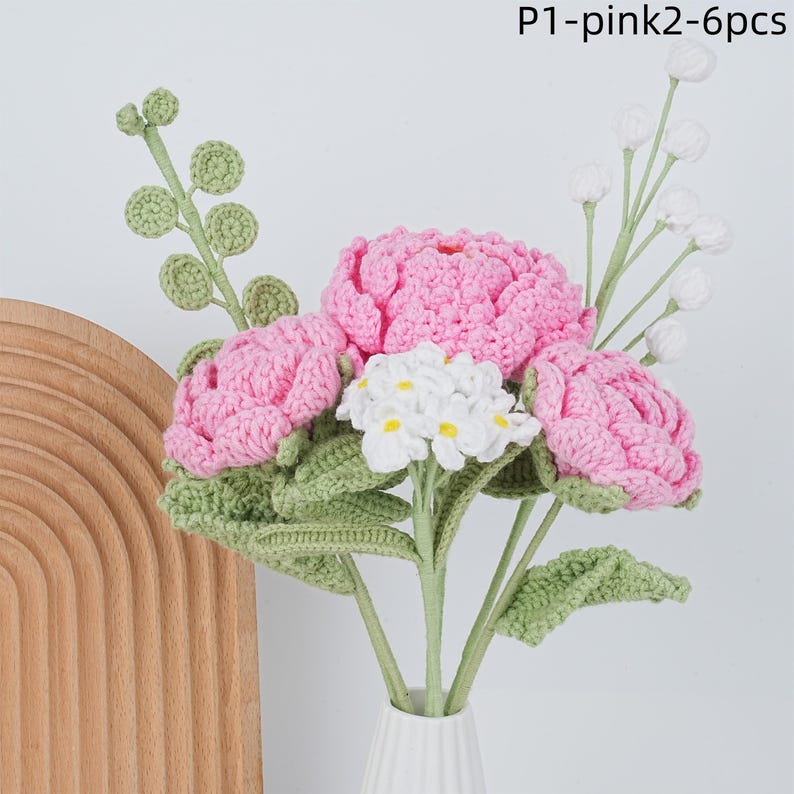 May include: A bouquet of six crocheted flowers in pink and white. The flowers are arranged in a vase and have green leaves.