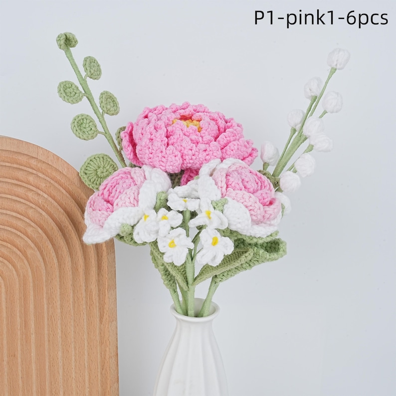 May include: A bouquet of crocheted flowers in pink and white, with green leaves, in a white vase. The flowers are arranged in a vase on a wooden surface. The text "P1-pink1-6pcs" is visible in the upper right corner of the image.