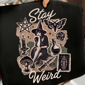 Könnte beinhalten: Schwarze Tragetasche mit einem Collage-Design mit einer Hexe, einer Motte, einem Pentagramm, einem Pilz, einer Kerze, einer Zaubertrankflasche, einem Dolch und den Worten "Stay Weird" im Vintage-Stil.