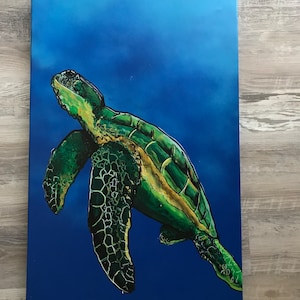 May include: A green sea turtle swimming in a blue ocean. The turtle has a green shell with yellow markings and is swimming with its head and flippers above the water.