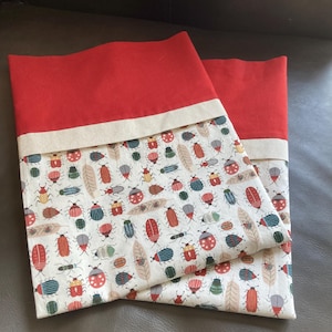 May include: Two red and white pillowcases with a bug pattern. The pillowcases have a red top border and a white bottom border.
