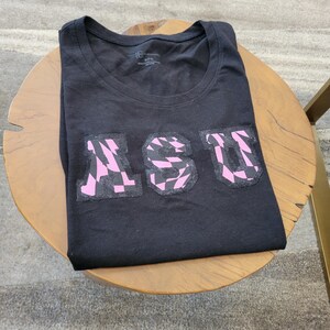 May include: Black t-shirt with a pink and black checkered "ASU" graphic.