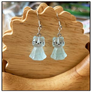 Puede incluir: Un par de pendientes de plata con forma de gato y un acabado translúcido azul claro.