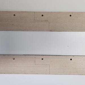May include: Two light-colored wooden planks with pre-drilled holes and interlocking joints. The planks are arranged parallel to each other against a white background. The wood grain is visible, and the planks appear to be part of a larger construction project.