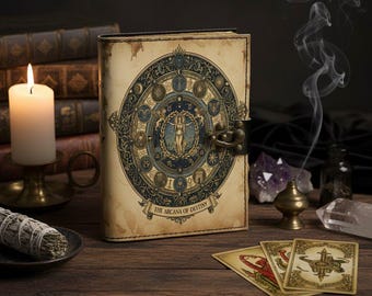 Peut inclure: Un journal de style vintage avec un motif circulaire détaillé représentant des symboles du zodiaque et une figure féminine centrale. Le journal est beige avec un fermoir en métal et le texte "THE ARCANA OF DESTINY". Des cartes de tarot et une bougie allumée sont également visibles.