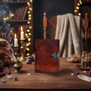 Puede incluir: Un diario de cuero marr&oacute;n con un cierre adornado descansa sobre una mesa de madera, rodeado de velas, libros y botellas de pociones. Una pluma descansa en un tintero de lat&oacute;n, con humo ascendente. La escena evoca un tema m&iacute;stico o de fantas&iacute;a.