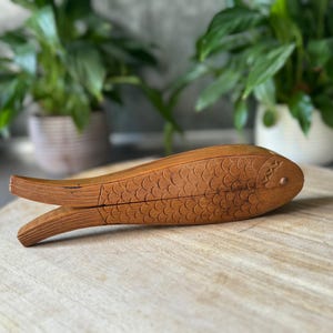 May include: A wooden fish-shaped box with a carved design of scales. The box is open and the inside is visible.