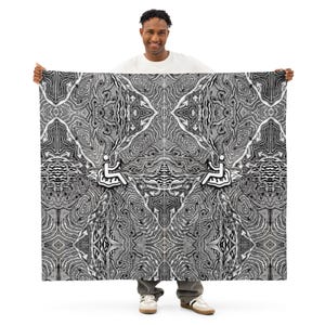 May include: A large, rectangular black and white patterned blanket. The design features a symmetrical pattern with abstract shapes and a wheelchair symbol. The blanket is held up by a person.