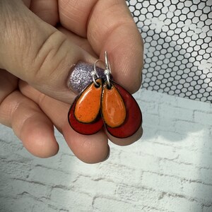 Può includere: Un paio di orecchini a forma di goccia con un design a strati. Gli orecchini sono realizzati in smalto rosso e arancione e hanno ganci d'argento.