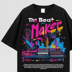 May include: Black t-shirt with a colorful graphic design. The design features the text "The Beat Maker" in white and pink, with a cityscape and music equipment illustration. The shirt has a crew neck and short sleeves.