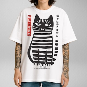 May include: White t-shirt with a black and white illustration of a cat. The text on the shirt reads "猫ではありません 私は三本足の I am not a three legged cat."