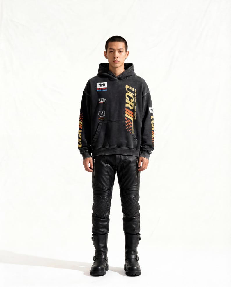 May include: A black hoodie with racing-themed graphics and patches, paired with black leather pants and boots. The hoodie features the number "11" and the text "UCR" in gold and red. The pants have quilted knee panels.