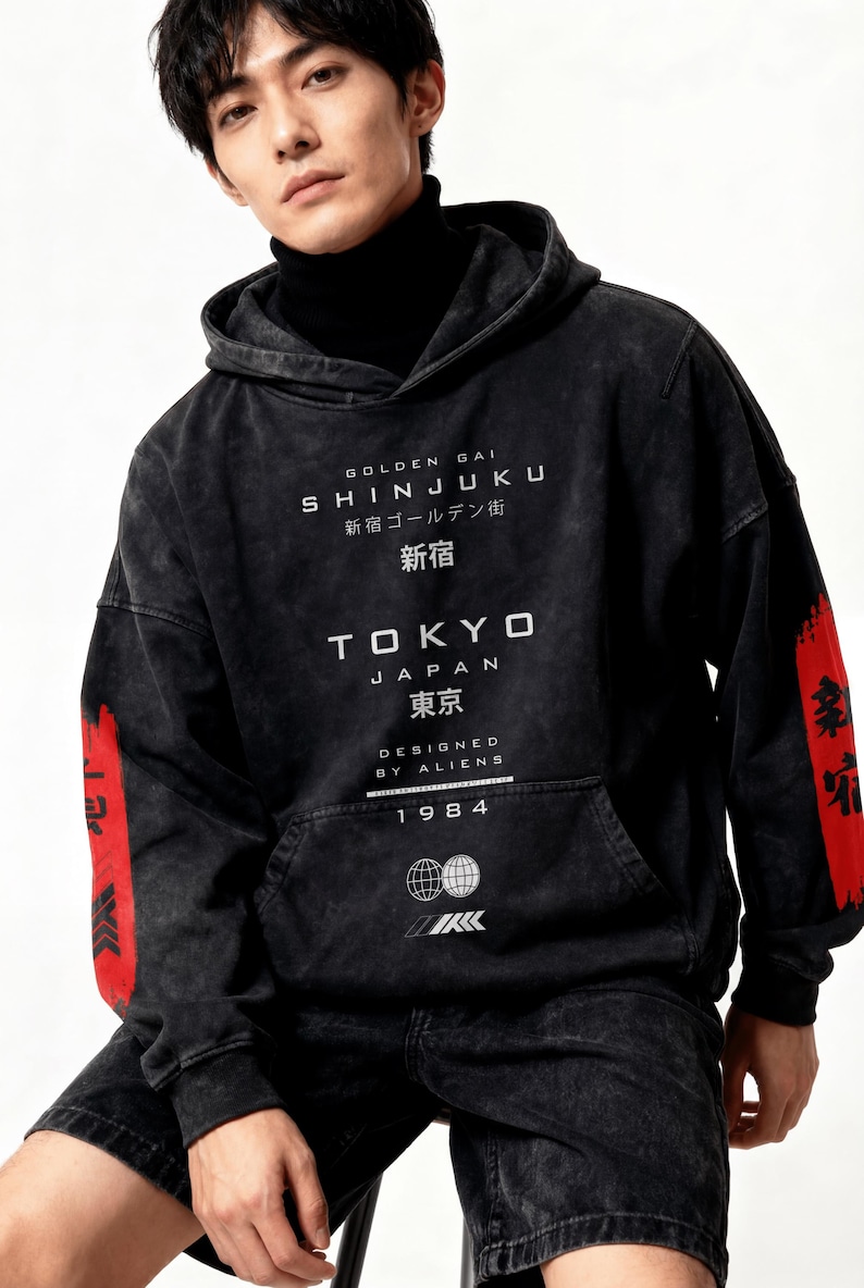 May include: Black hoodie with white text reading "GOLDEN GAI SHINJUKU 新宿 TOKYO JAPAN 東京 DESIGNED BY ALIENS 1984". Red accents with Japanese text adorn the sleeves. Features a front pocket and drawstring hood.
