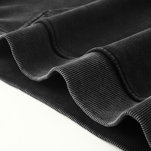May include: A charcoal black sweatshirt featuring a thick, ribbed knit hem and cuffs. The fabric has a soft, slightly faded texture, showcasing the detailed stitching along the seams where the ribbed trim meets the main body of the garment.
