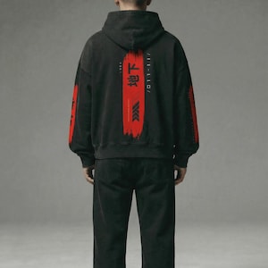 May include: Black hoodie and trousers. The hoodie has red Japanese text and a red brushstroke design on the back, with red accents on the sleeves. The outfit is worn by a person.