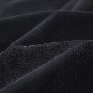 May include: Close-up of black fabric with visible texture and folds. The material appears soft and drapes naturally, suggesting a garment or textile. The dark colour and subtle variations in light create depth.