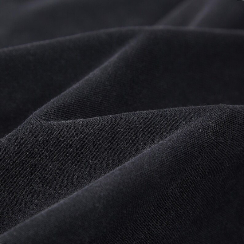 May include: Close-up of black fabric with visible texture and folds. The material appears soft and drapes naturally, suggesting a garment or textile. The dark colour and subtle variations in light create depth.