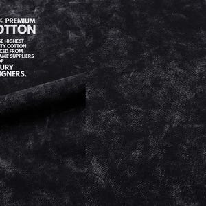 May include: Close-up of black fabric with a textured, mottled appearance. White text reads "100% PREMIUM COTTON" and additional text stating the cotton is sourced from the same suppliers as luxury designers.