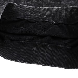 May include: Close-up of a black sweatshirt with a distressed, textured appearance. The ribbed neckline and hem are visible, with a faded, worn look. The fabric appears to be a heavy knit, suitable for cooler weather.