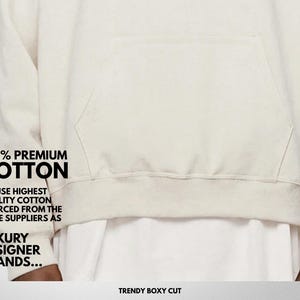 Pu&ograve; includere: Felpa con cappuccio color crema con tasca frontale e la scritta "100% PREMIUM COTTON". La felpa &egrave; realizzata in un materiale morbido e ha un taglio squadrato alla moda. Il testo menziona anche l'uso di cotone di alta qualit&agrave;.