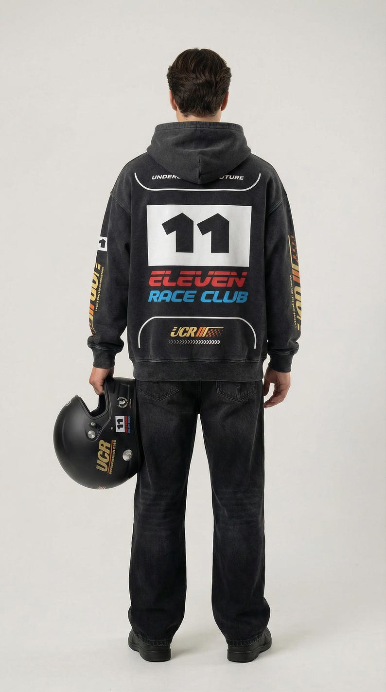 May include: A person wearing a black hoodie and jeans, holding a black helmet. The hoodie features the number 11, "ELEVEN RACE CLUB" text, and "UCR" branding. The helmet also has "UCR" branding.