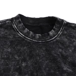 May include: Close-up of a black crew neck sweatshirt with a distressed, acid wash effect. The collar and neckline are ribbed, and the fabric has a textured appearance. The garment is a dark, neutral color.