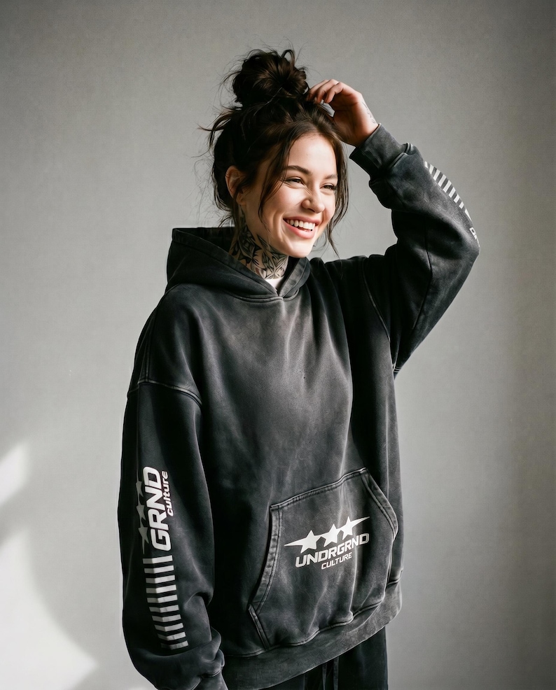 May include: A dark gray hoodie with the text "GRND culture" printed vertically on the left sleeve and "UNDRGRND culture" with three stars on the front pocket. The hoodie has a drawstring hood and a kangaroo pocket.