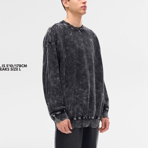 May include: A dark gray, acid-wash style sweatshirt with long sleeves. The garment has a crew neck and ribbed cuffs and hem. The model in the image is 5'10" (178cm) and wears a size L.
