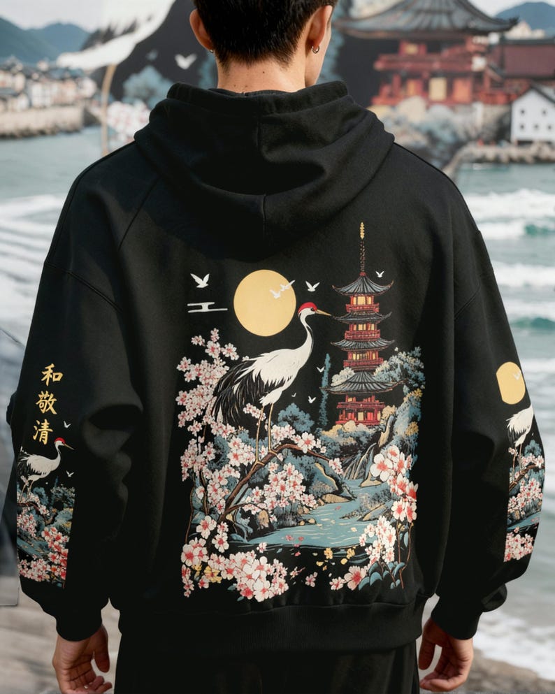 May include: Black hooded sweatshirt with a Japanese-inspired design. The back features a crane, pagoda, and floral elements in a scenic illustration. The sleeves have additional crane and floral details. The text "和敬清" is printed on the left sleeve.