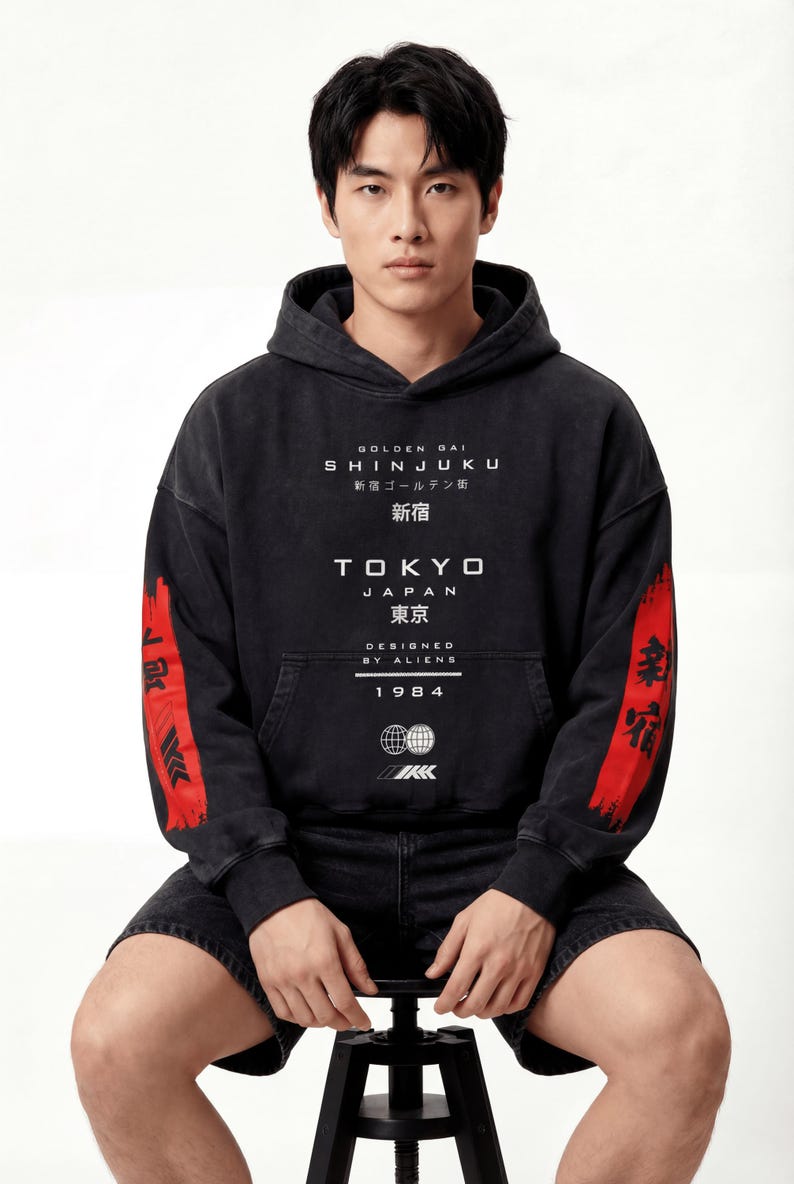 May include: Black hoodie with white text: "Golden Gai Shinjuku Tokyo Japan" and "Designed by Aliens 1984". Red stripe with Japanese text on the sleeves. The hoodie has a kangaroo pocket and a drawstring hood.