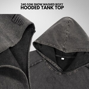 May include: A gray hooded tank top with a boxy fit. The top is made of a soft, washed cotton fabric. The hood is lined with a black fabric. The text "240 GSM SNOW WASHED BOXY HOODED TANK TOP" is printed on the top.