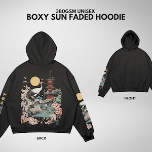 May include: Black boxy hoodie with a Japanese-inspired design. The back features a crane, pagoda, and floral elements. Sleeves have matching artwork. The front view shows a plain black hoodie. Text on the hoodie reads "380GSM UNISEX BOXY SUN FADED HOODIE".