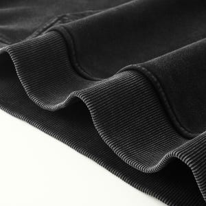 May include: A charcoal black sweatshirt featuring a thick, ribbed knit hem and cuffs. The fabric has a soft, slightly faded texture, showcasing the detailed stitching along the seams where the ribbed trim meets the main body of the garment.