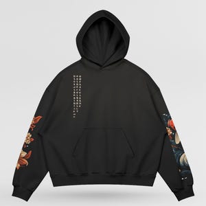 Pu&ograve; includere: Felpa con cappuccio nera con cappuccio con coulisse e tasca a marsupio. Le maniche presentano disegni floreali nei toni del rosso, arancione e crema. Testo verticale stampato sul petto sinistro. Felpa casual e oversize.