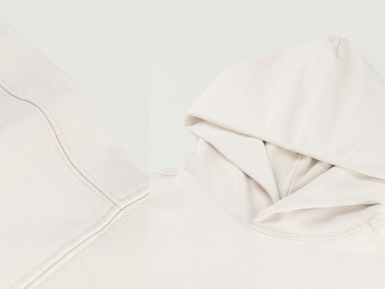 Pu&ograve; includere: Primo piano di una felpa con cappuccio color crema, che mostra il cappuccio e lo scollo. Il tessuto appare morbido e le cuciture sono visibili. La felpa con cappuccio &egrave; di un colore neutro, adatta a vari outfit.