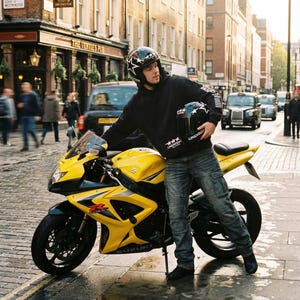 May include: A yellow Suzuki GSX-R motorcycle parked on a wet cobblestone street. The motorcycle has black accents and a black tire. A person wearing a black helmet with star designs and a black hoodie stands next to the motorcycle.