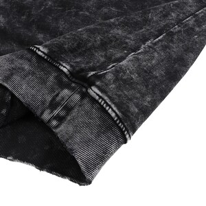 May include: Close-up of a black garment with a distressed, acid-wash effect. The fabric has a textured appearance with visible seams and a ribbed cuff. The overall aesthetic is dark and edgy, suggesting a casual wear item.