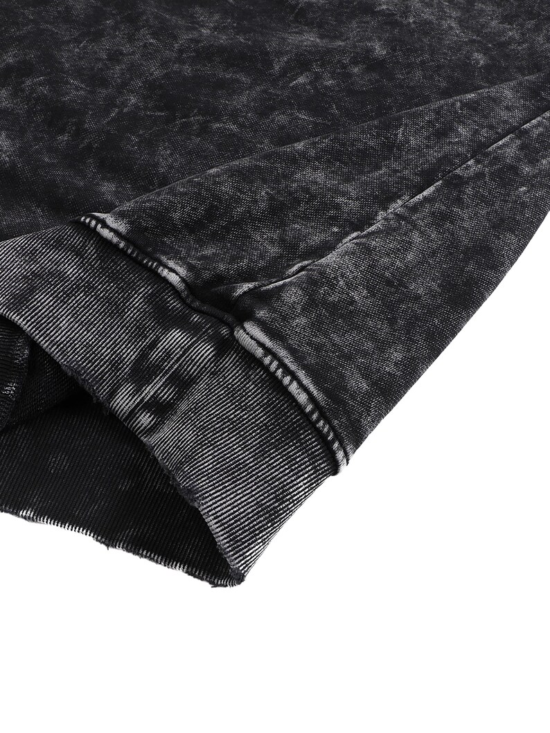 May include: Close-up of a black garment with a distressed, acid-wash effect. The fabric has a textured appearance with visible seams and a ribbed cuff. The overall aesthetic is dark and edgy, suggesting a casual wear item.