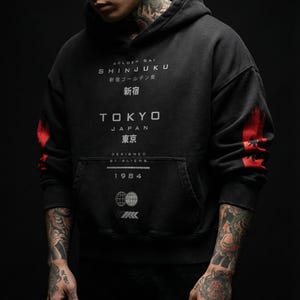 May include: Black hoodie with white and red graphics. The front of the hoodie features the text "GOLDEN GAI SHINJUKU" and "TOKYO JAPAN". The sleeves have red accents. The hoodie also has a front pocket and the year "1984" printed on it.