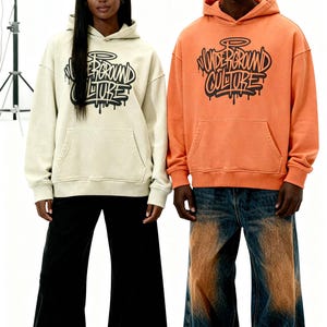 May include: A cream-colored hoodie and an orange hoodie, both featuring a black graphic print that reads "UNDERGROUND CULTURE" in a stylized graffiti font. Each hoodie includes a front kangaroo pocket and a hood with matching drawstrings.