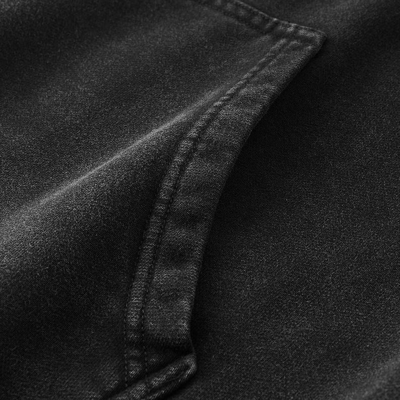 May include: A charcoal black hoodie featuring a washed, faded fabric texture. The garment includes a prominent kangaroo pocket on the front, defined by thick, reinforced double-stitched seams along the edges of the pocket opening.