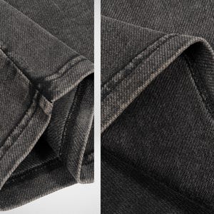 May include: Close-up of the dark gray denim fabric of a pair of jeans. The fabric has a textured, woven appearance and is stitched with a double seam.