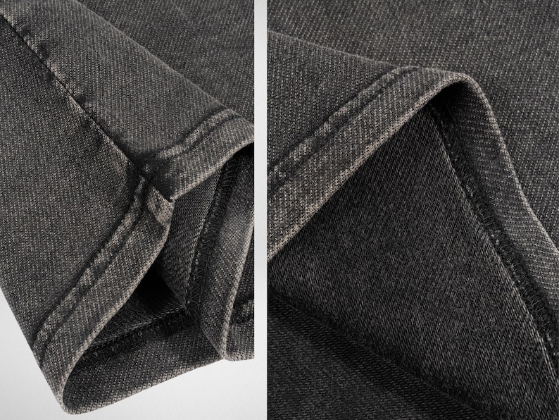 May include: Close-up of the dark gray denim fabric of a pair of jeans. The fabric has a textured, woven appearance and is stitched with a double seam.