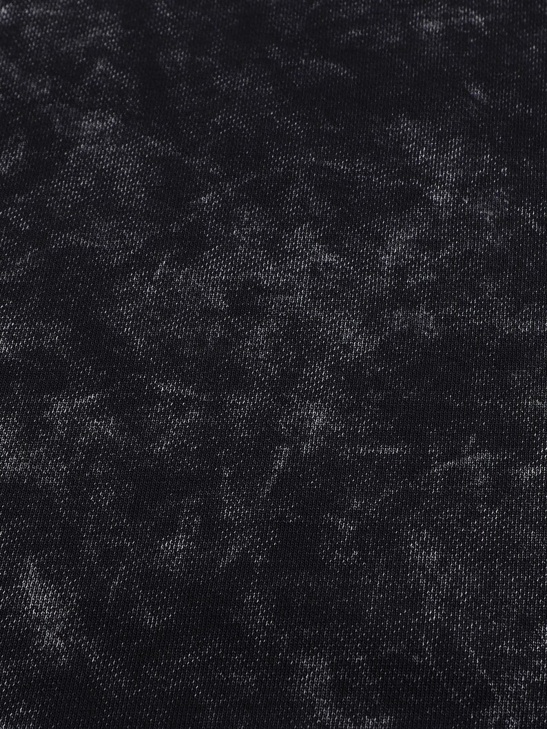 May include: Close-up of a black fabric with a textured, mottled appearance. The fabric has a dark base color with lighter, faded areas creating a distressed effect. The texture appears to be a woven material.