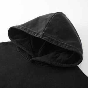 May include: A solid black hooded sweatshirt featuring a washed-out, faded aesthetic on the exterior fabric. The hood is double-layered with a deep, dark interior lining and visible stitching along the edges of the hood opening and seams.
