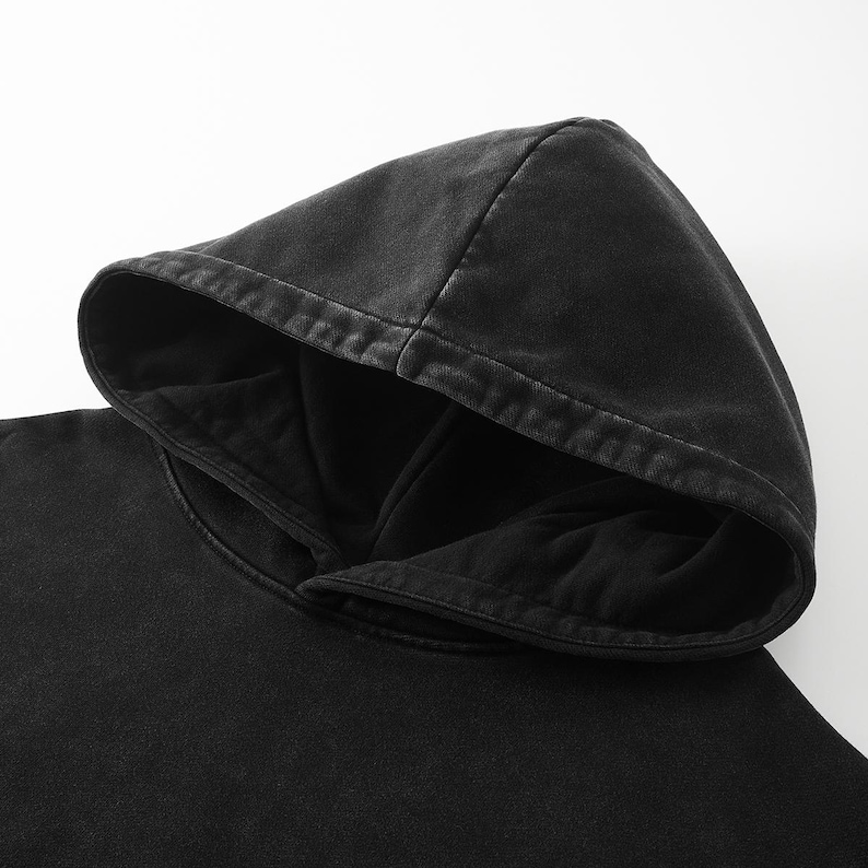 May include: A solid black hooded sweatshirt featuring a washed-out, faded aesthetic on the exterior fabric. The hood is double-layered with a deep, dark interior lining and visible stitching along the edges of the hood opening and seams.