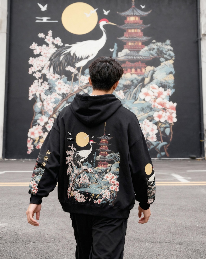 May include: Black hoodie featuring a Japanese-inspired design with a crane, pagoda, cherry blossoms, and a full moon. The sleeves have additional moon and crane details. The back of the hoodie showcases a detailed landscape scene.