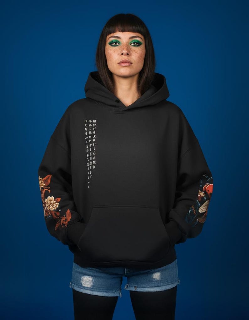 Pu&ograve; includere: Felpa con cappuccio nera con tasca frontale e cappuccio con coulisse. Le maniche presentano disegni floreali e di pesci koi. Il testo giapponese &egrave; stampato verticalmente sul lato sinistro. La modella indossa pantaloncini di jeans blu.